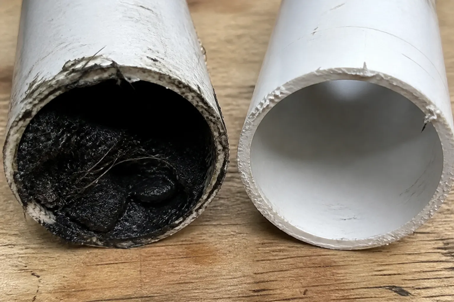 Clogged drain pipe next to a scoured-clean pipe after drain cleaning