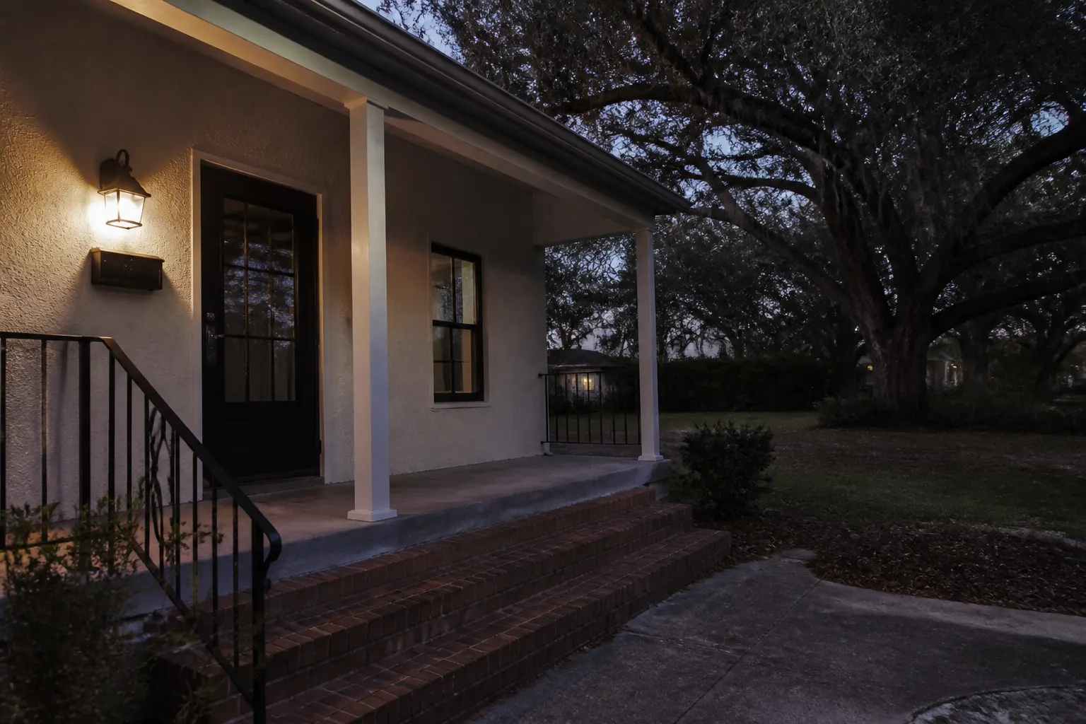 Wet-rated porch wall sconce glowing at dusk on an empty Tampa bungalow