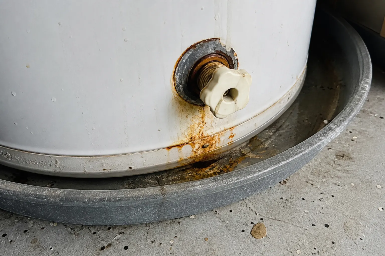Rusty sediment and a wet drain pan under a tank water heater
